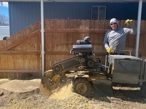 Carey Cordova posing with a stump grinder on a job site with wood chips visible